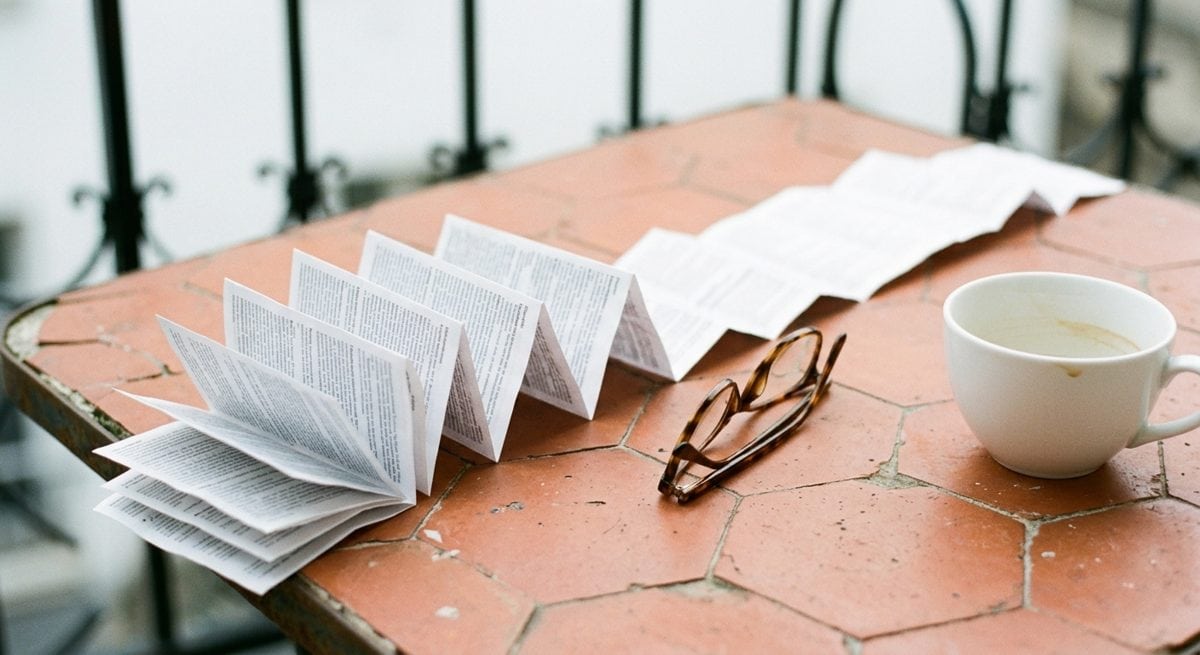 Notice de médicament dépliée en accordéon sur une table de balcon en tomettes, avec une paire de lunettes de lecture